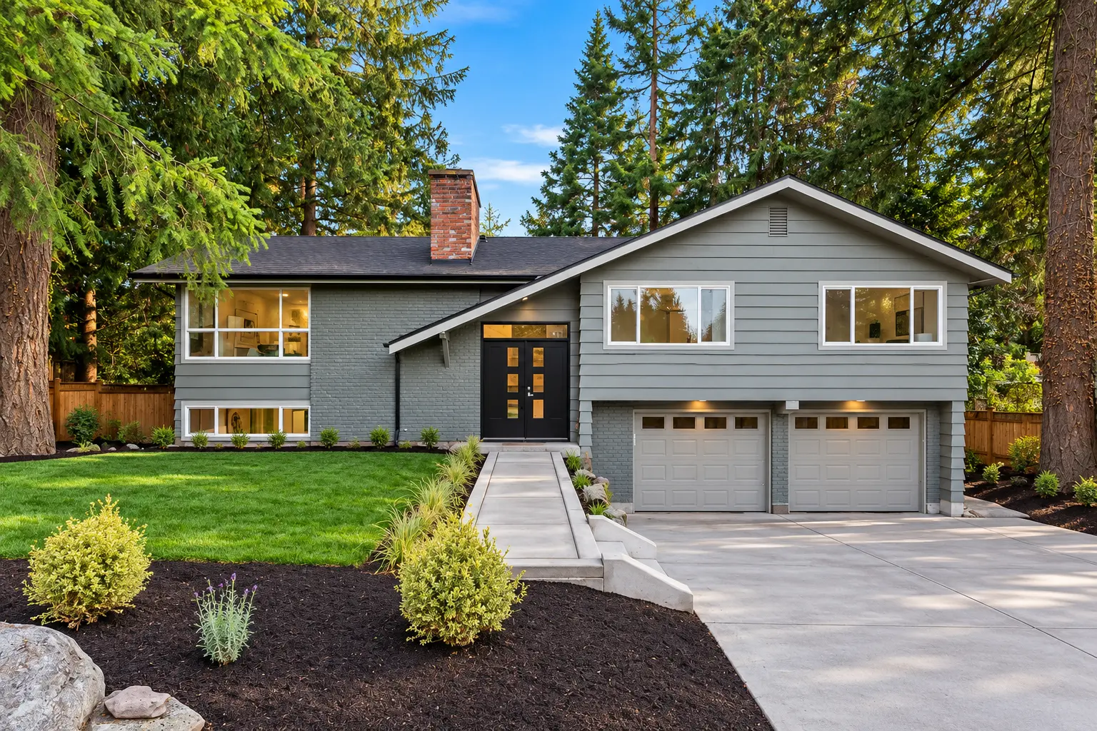 Same split-level home after renovation with charcoal-gray siding and brick, matching garage doors, a new concrete driveway and landscaped front yard