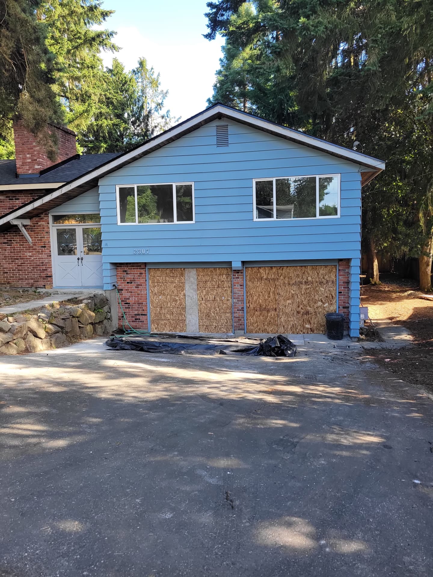 Split-level home before renovation with blue siding, unpainted brick and boarded-over garage door openings