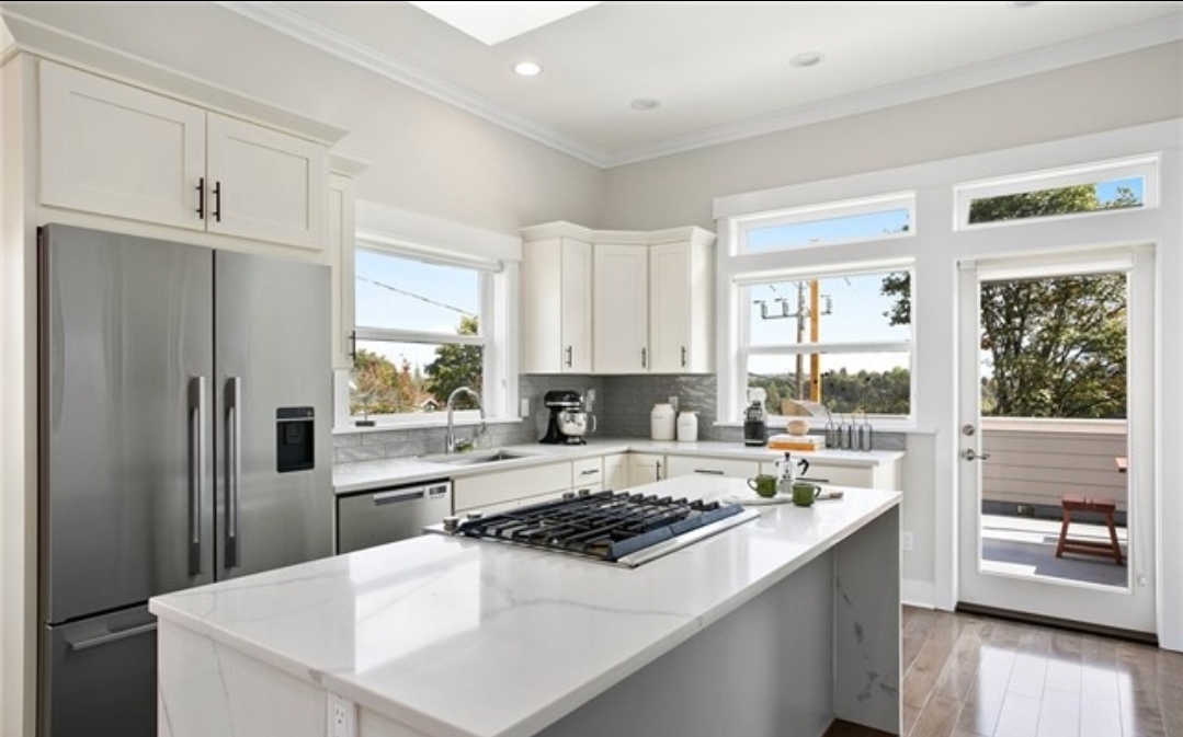 Remodeled kitchen with off-white shaker cabinets, white waterfall island and a glass door opening to an outdoor deck